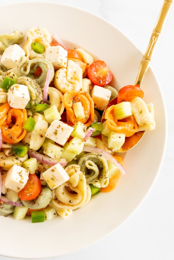 A close-up of a bowl of tortellini salad with colorful vegetables, diced cheese, and a golden fork—one of the perfect BBQ sides for your summer gatherings.