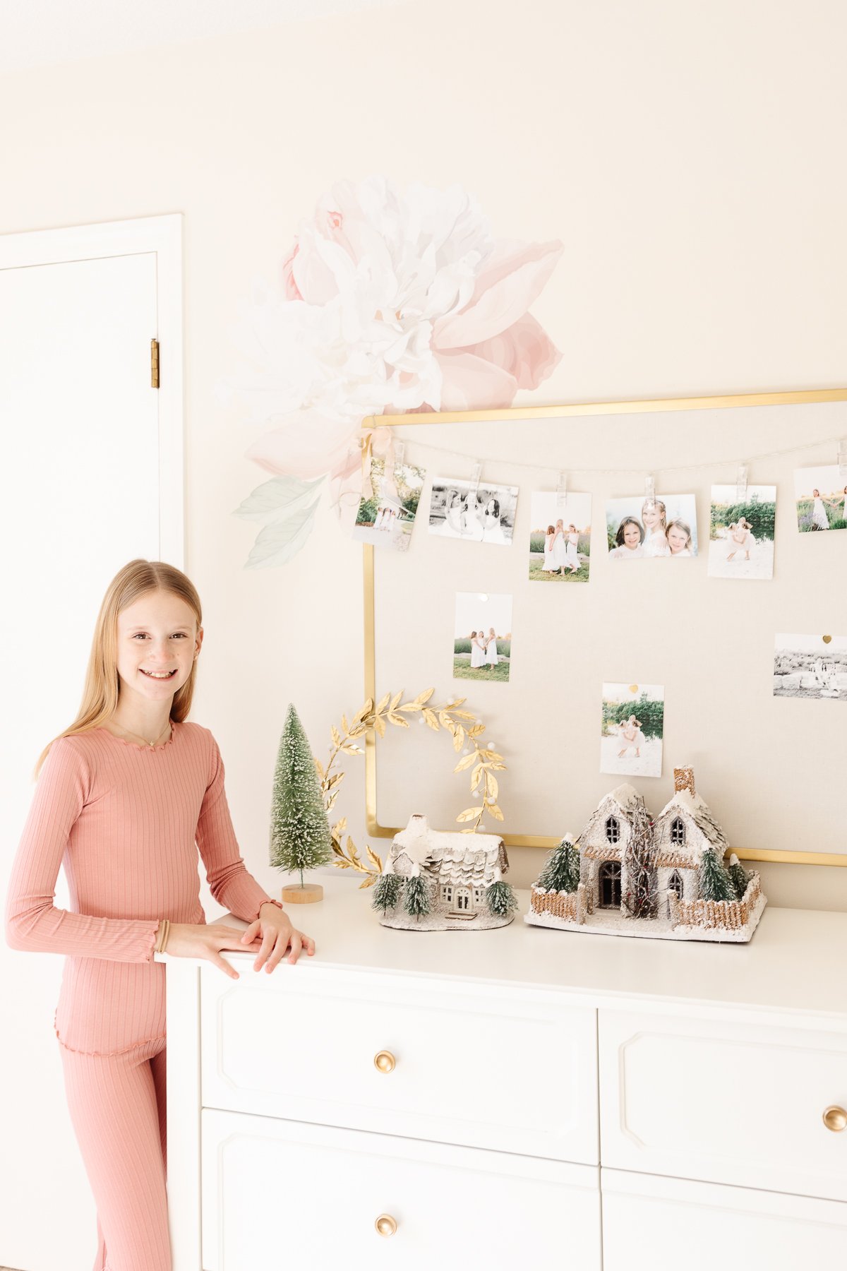 girl next to dresser with gold pin board and flower on wall