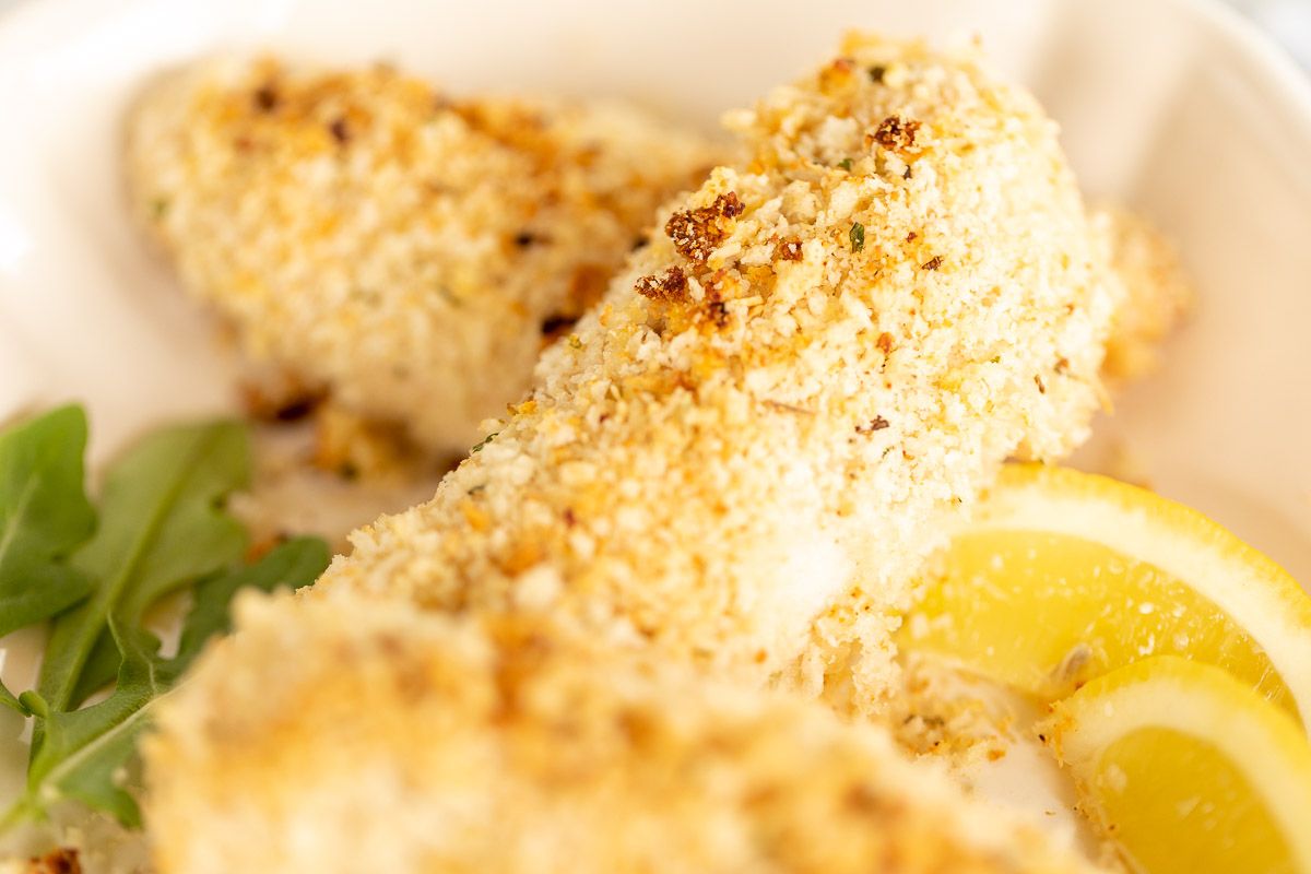 A close up of baked panko chicken, lemon slices for garnish