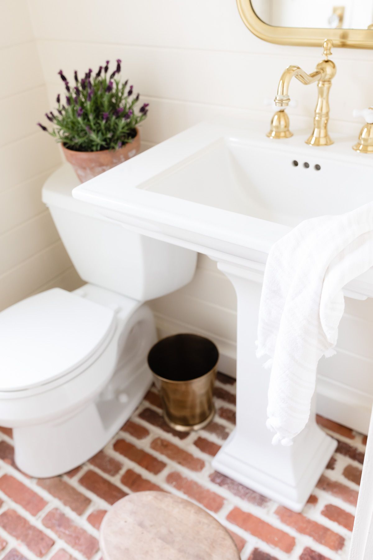 A small bathroom with brick floors and a pedestal sink