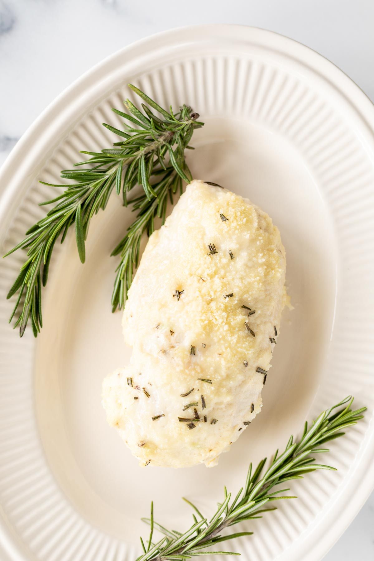 Mayo chicken, garnished with fresh rosemary on an oval platter.