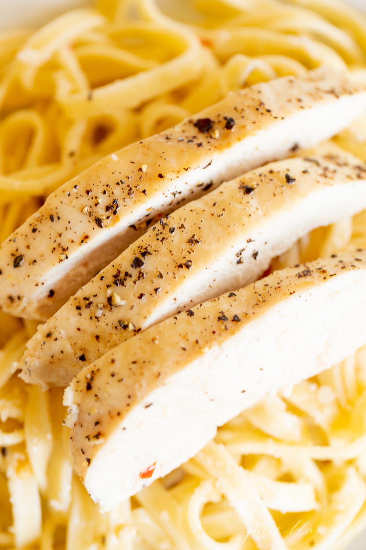 A chicken pasta recipe with baked chicken breast cut into strips over a bed of linguine. 