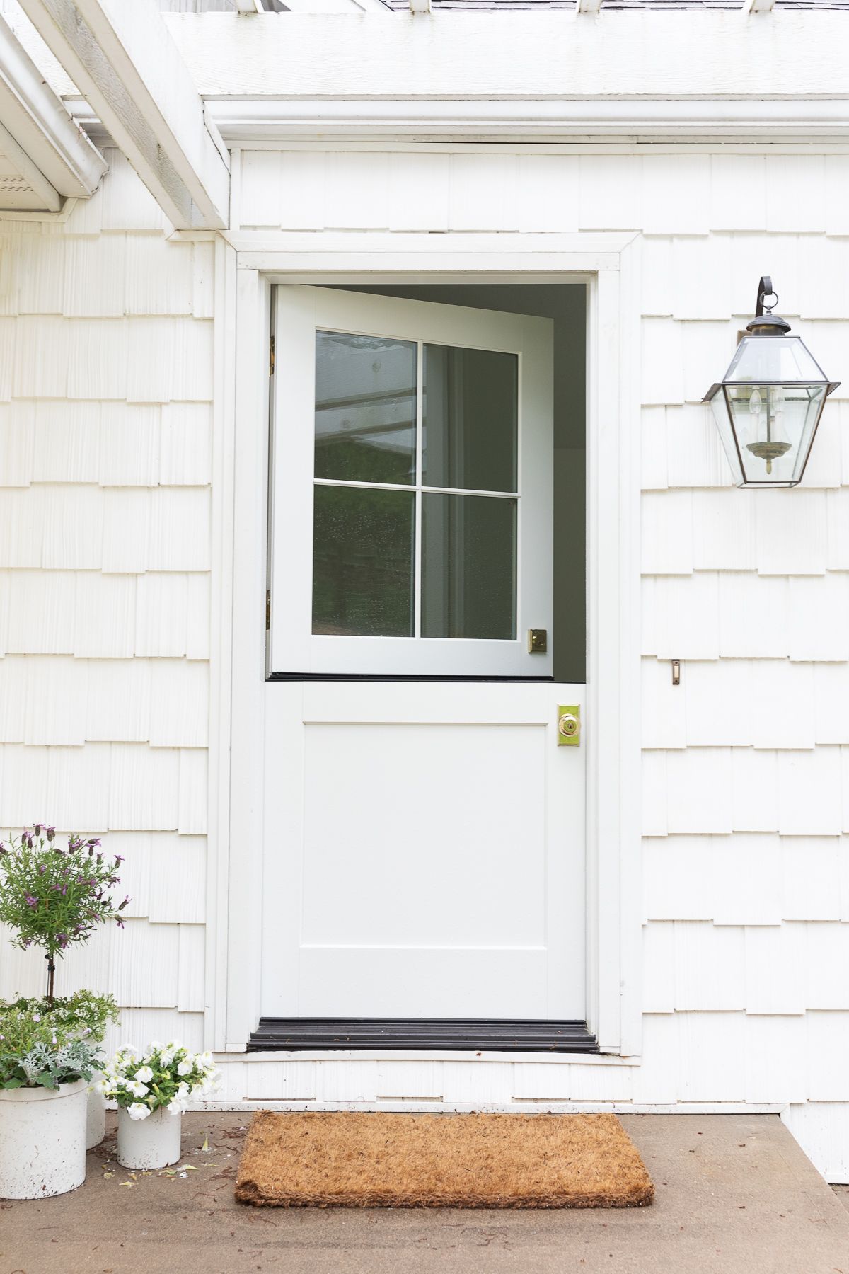 A white Dutch door with a wreath and brass Dutch door hardware