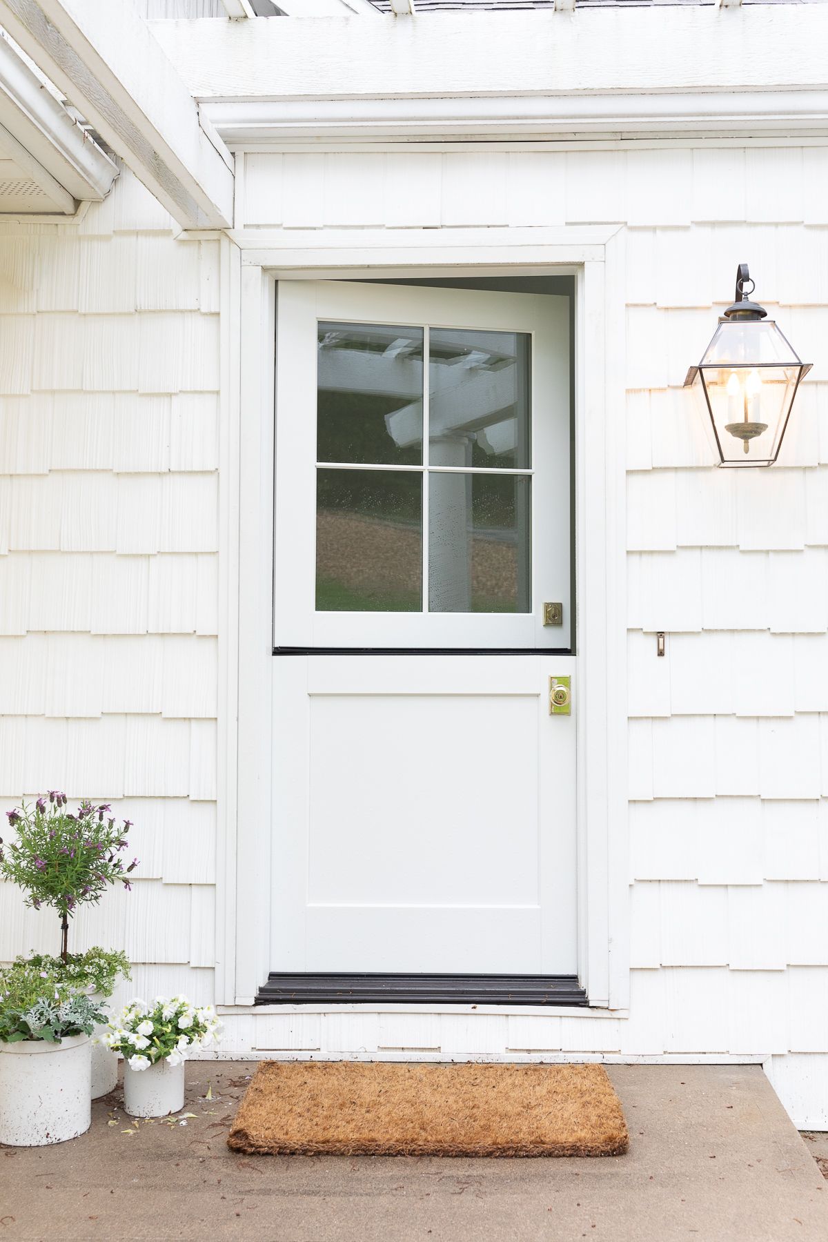 A white Dutch door with a wreath and brass Dutch door hardware