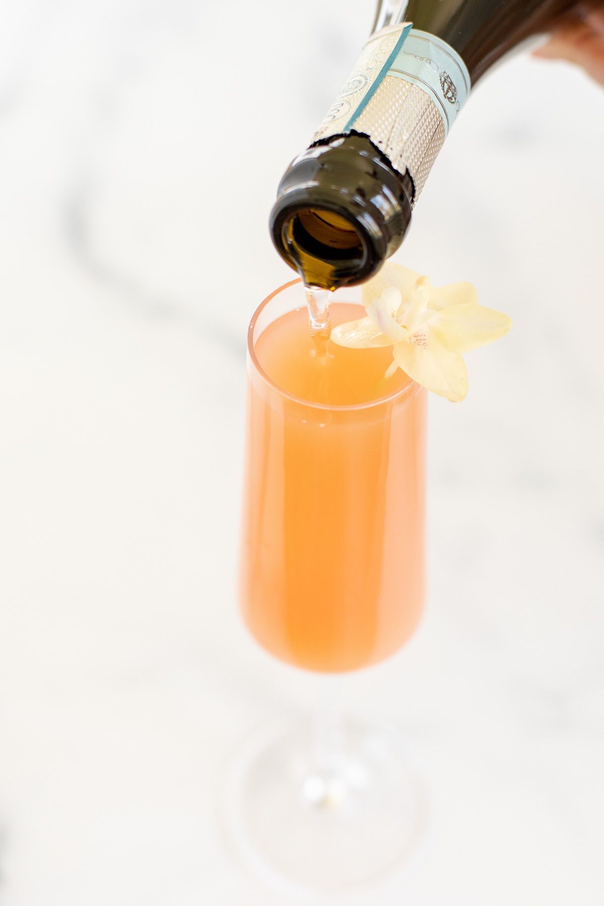 A grapefruit mimosa on a marble surface, garnished with a flower and a slice of grapefruit
