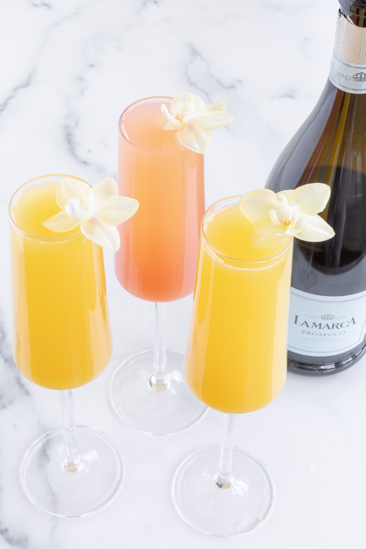 A group of three mimosas with a bottle of champagne in the background