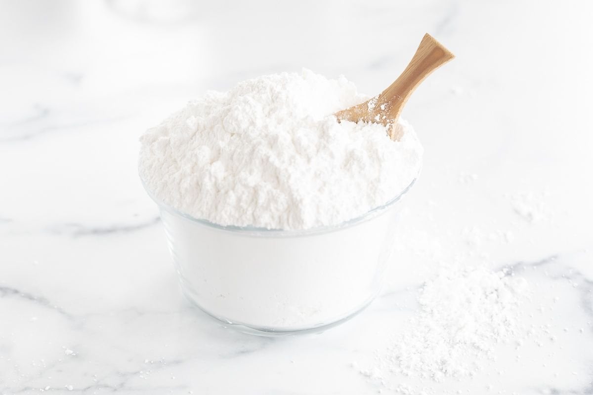 A glass bowl full of homemade powdered sugar with a small wooden spoon.