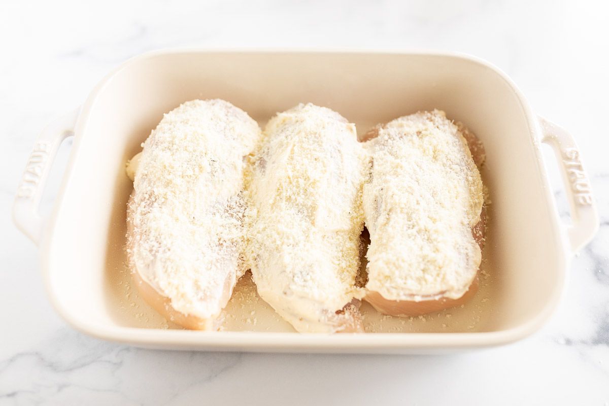 Three chicken breasts covered in mayonnaise in a white baking dish.