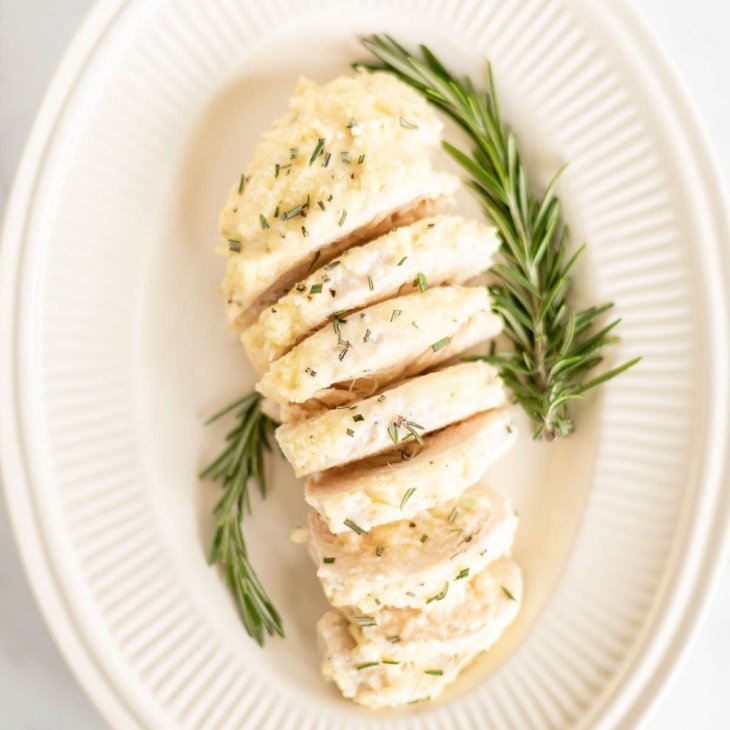 Sliced mayo chicken, garnished with fresh rosemary on an oval platter.