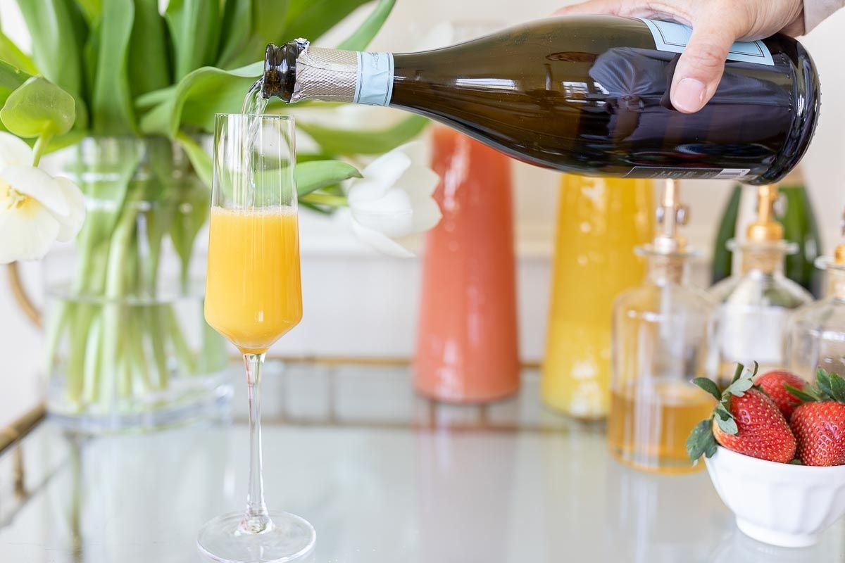 A hand pouring champagne into a glass on a mimosa bar