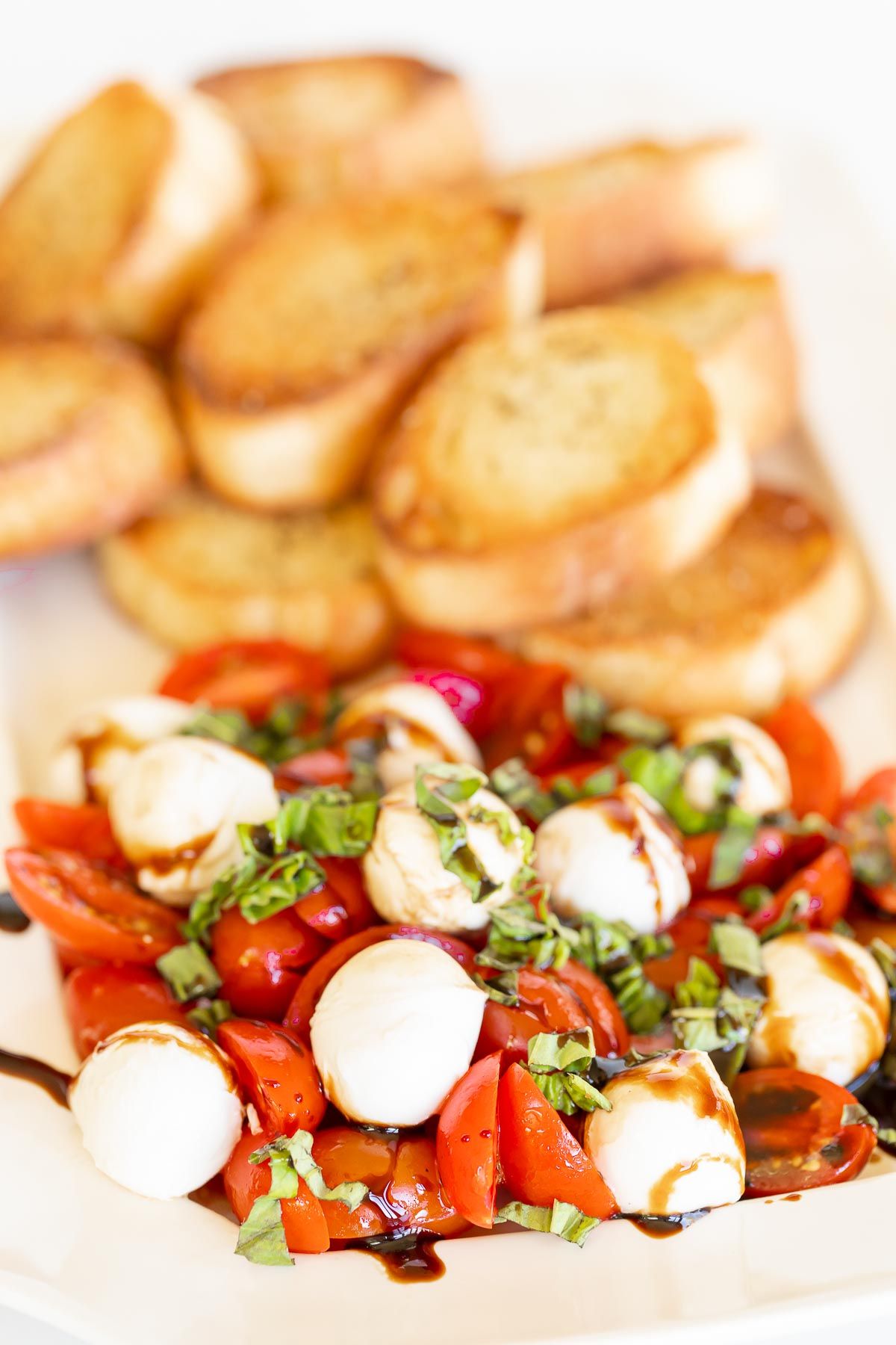 Sliced tomatoes, pearls of mozzarella, topped with basil and balsamic, crostini in the background