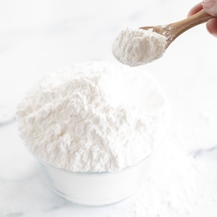 A glass bowl full of homemade powdered sugar with a small wooden spoon.