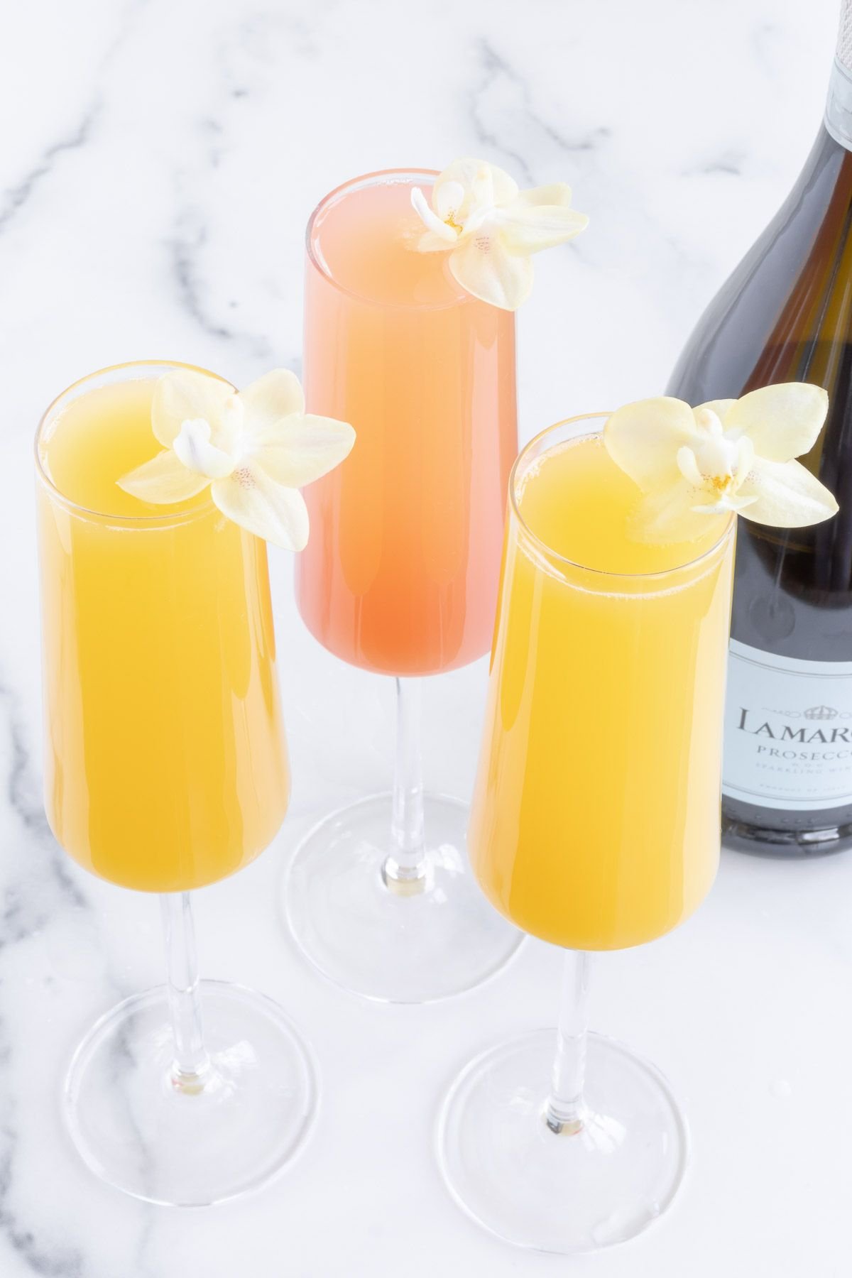 prosecco mimosas garnished with flowers on a marble surface.