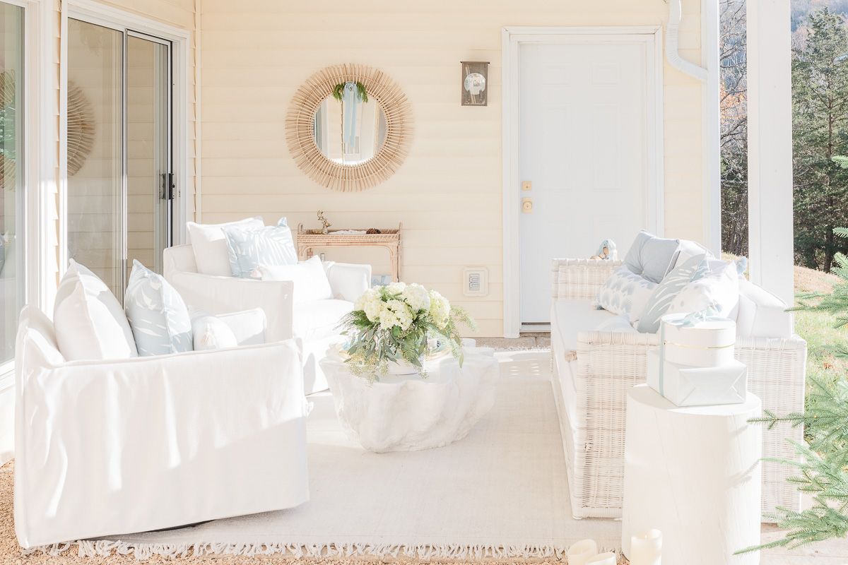 An outdoor patio with white sofas and chairs and a rattan mirror