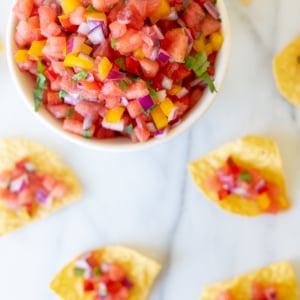 A bowl of fresh tomato salsa recipes surrounded by tortilla chips on a marble surface.