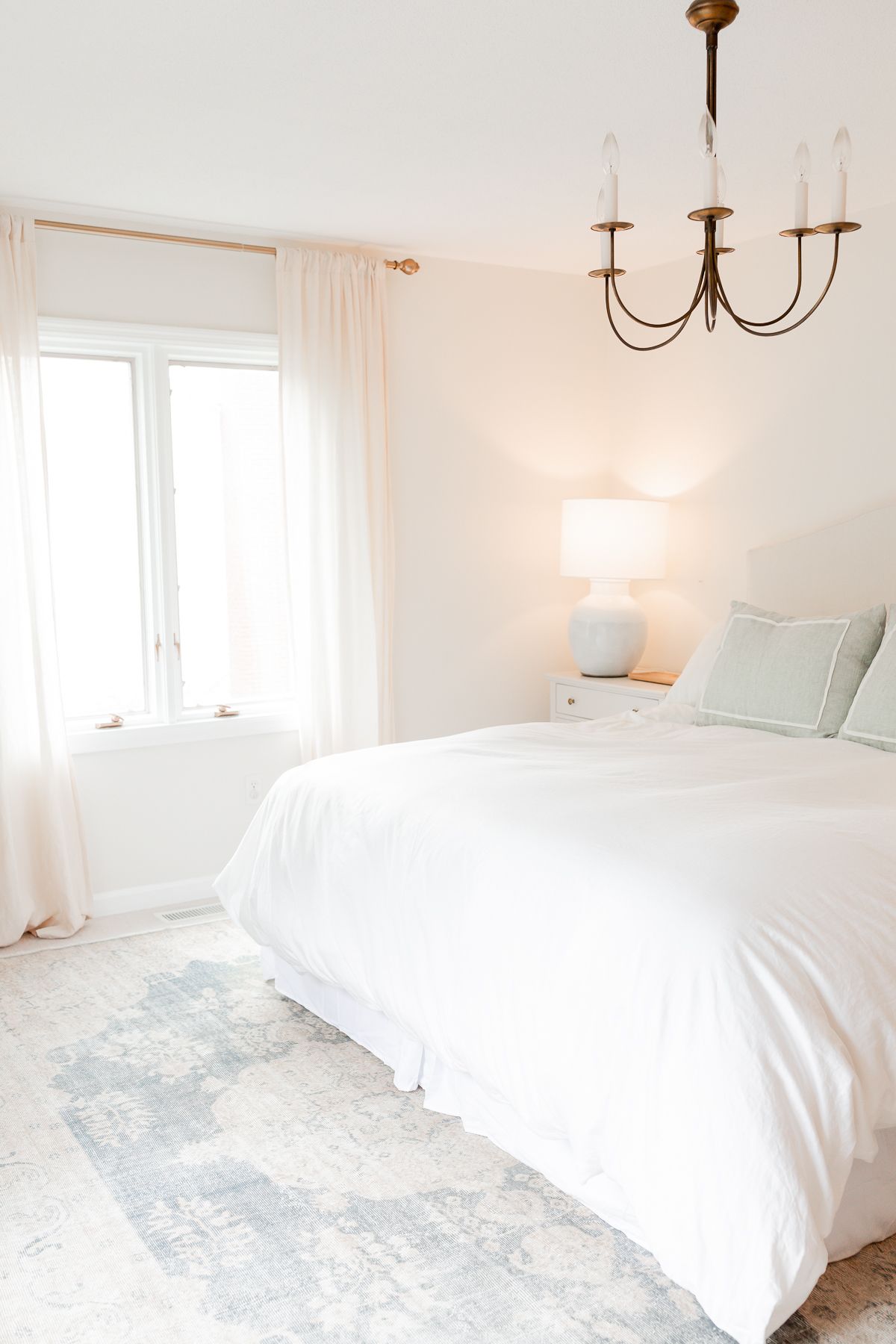 A white bedroom with blue traditional rugs on the floor