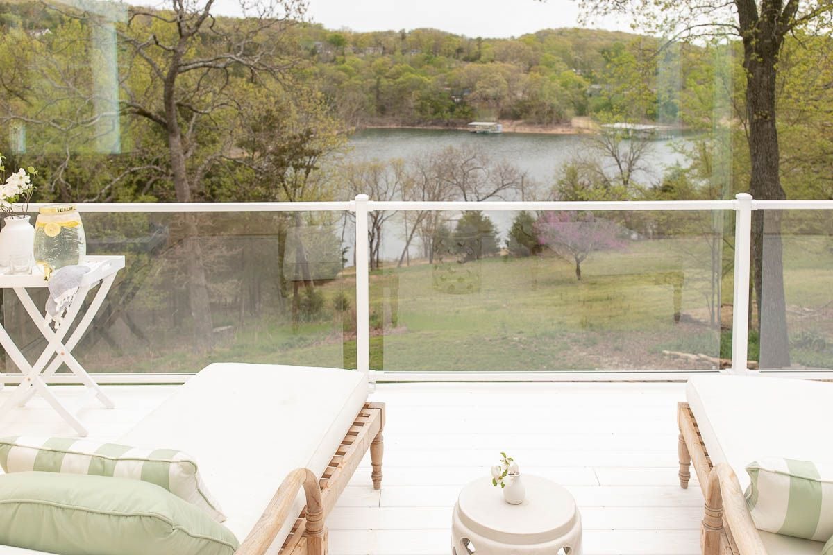 A white deck with glass balustrades, with two wooden benches and a ceramic garden stool in the middle.