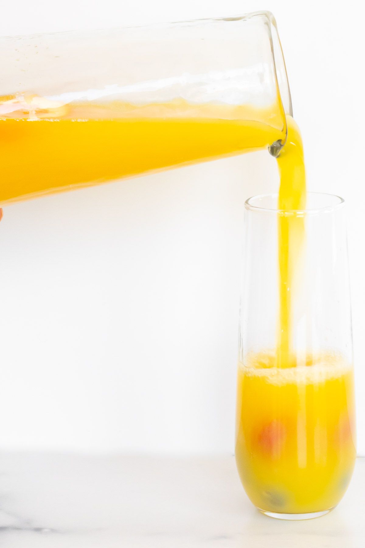 Bottomless mimosa pitcher pouring into a glass with fruit