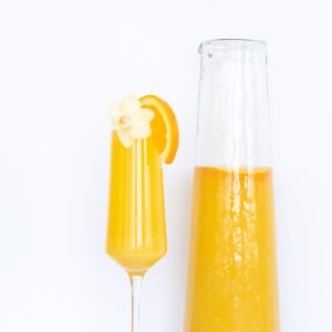A mimosa in a champagne glass, pitcher of mimosas to the side