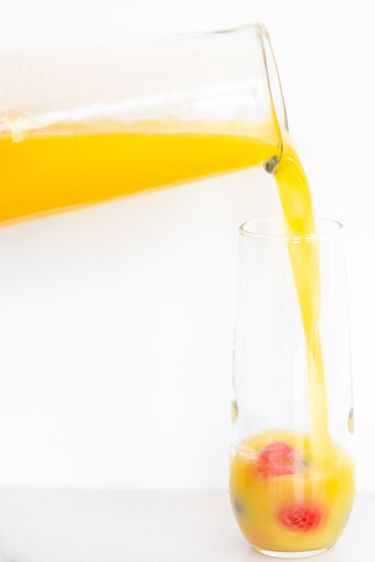 Bottomless mimosa pitcher pouring into a glass with fruit