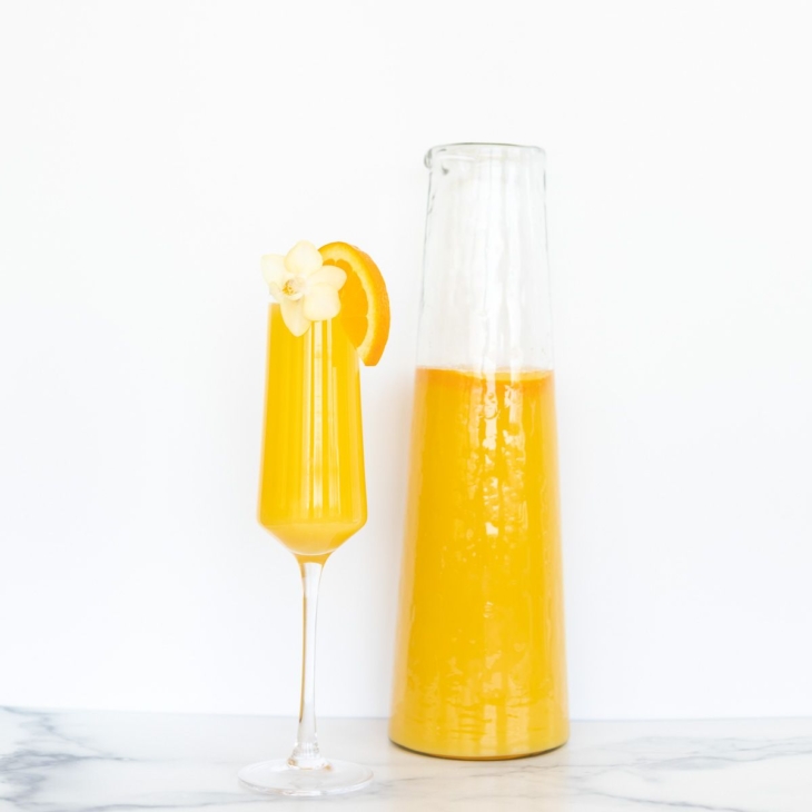 A glass pitcher of bottomless mimosas with a single flute of a mimosa to the side