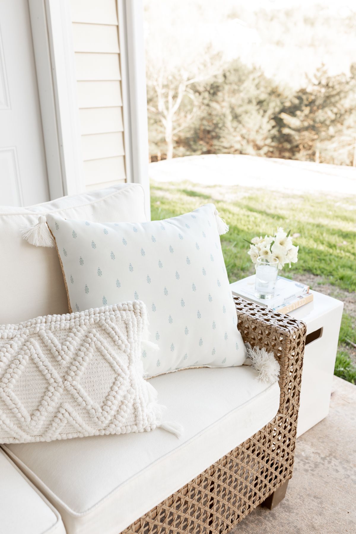 A patio with a wicker sectional and a white square ceramic garden stool