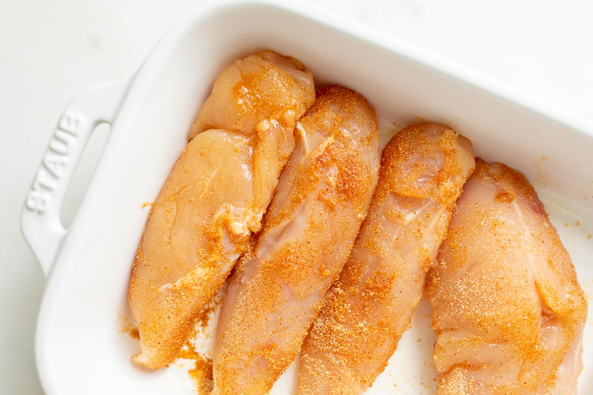 Chicken breasts with seasoning in a white baking pan