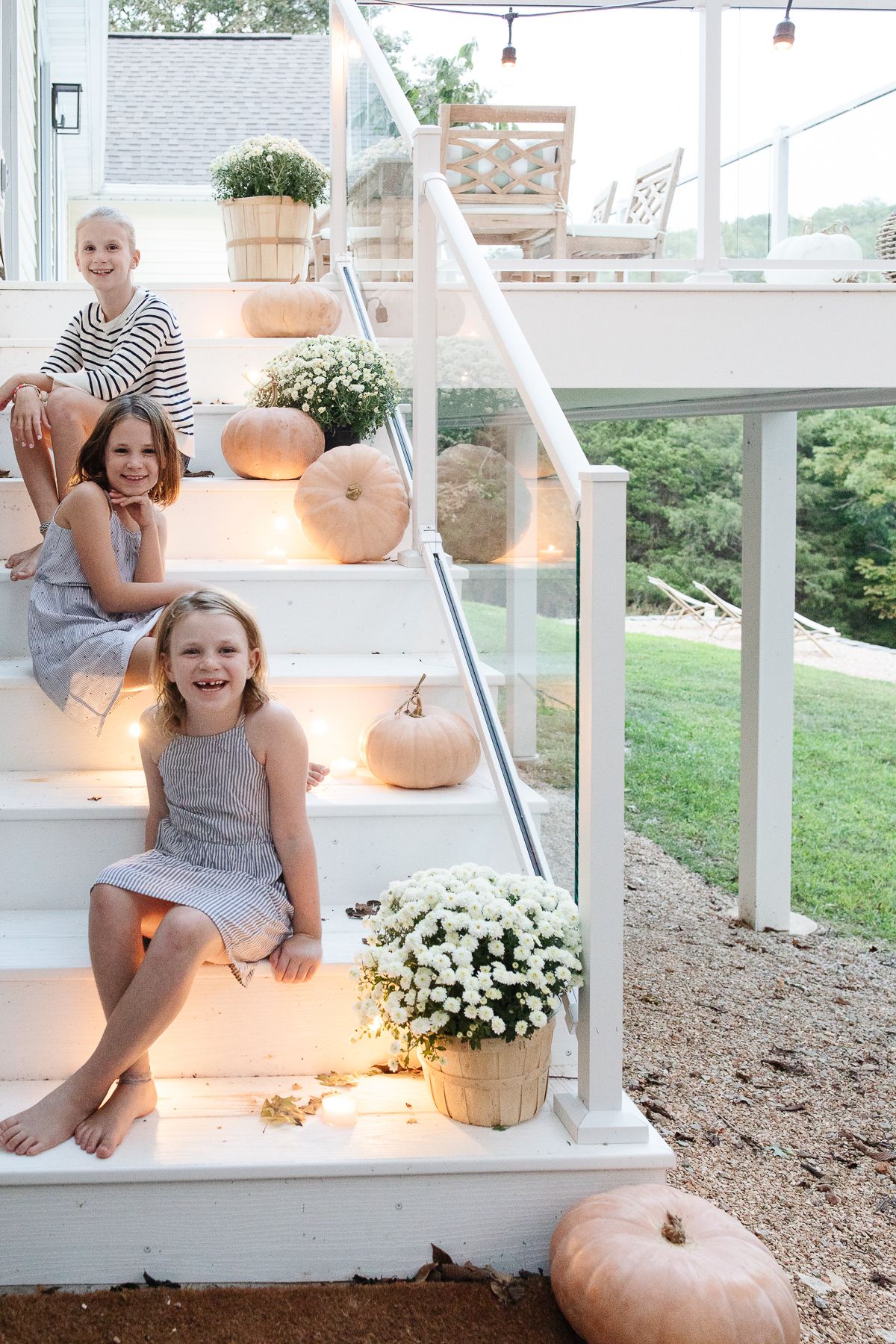 Three little girls on white deck steps decorated with pumpkins