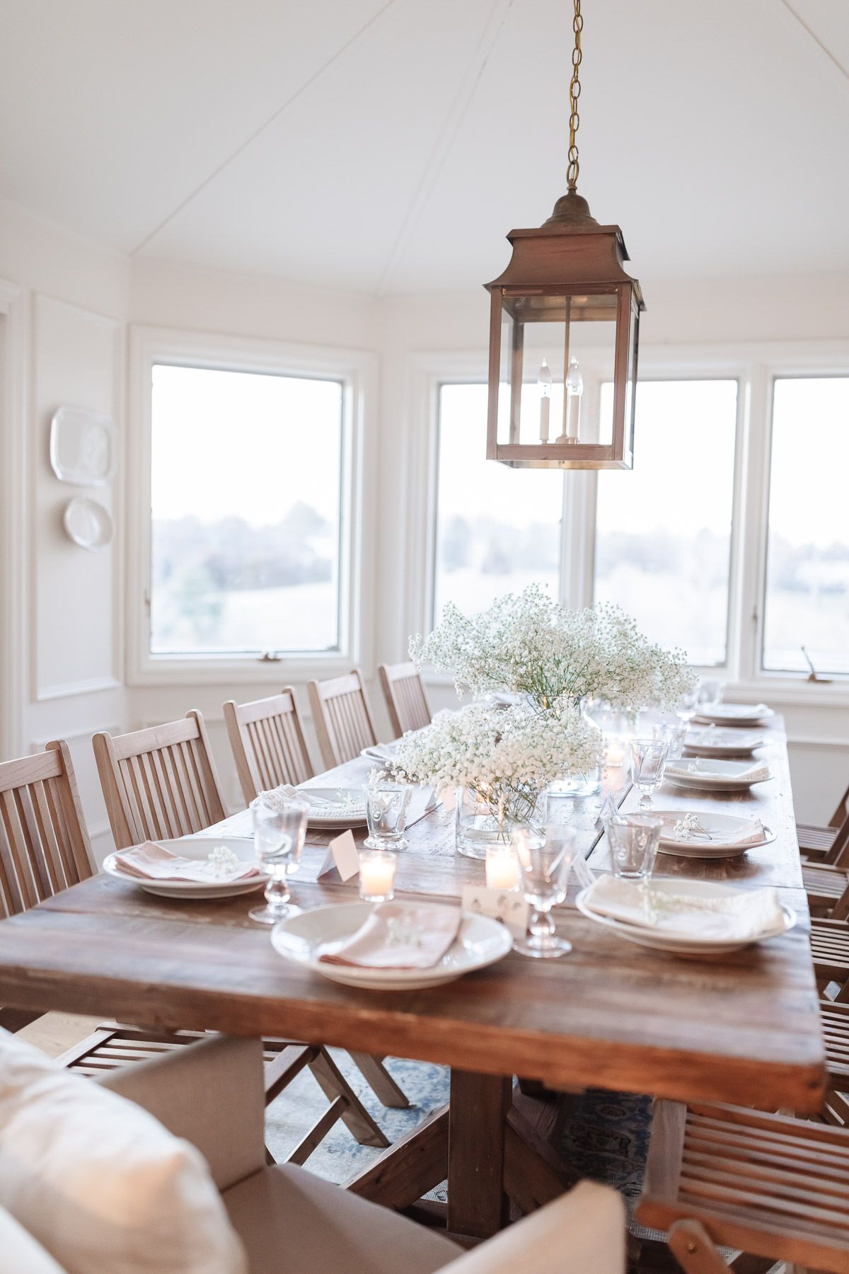 A farmhouse dining table surrounded by wood chairs in a white dining room