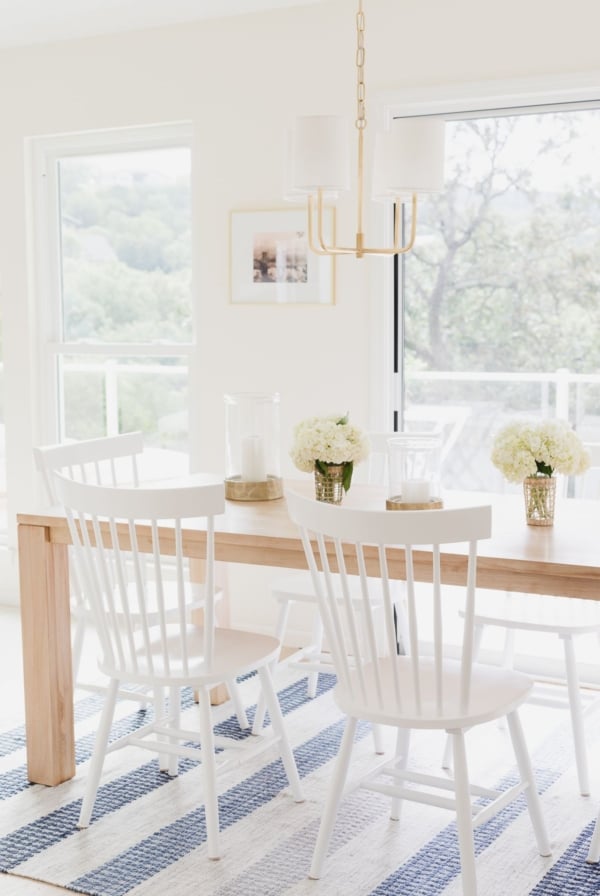 A teak dining table with white chairs on a blue and white striped rug