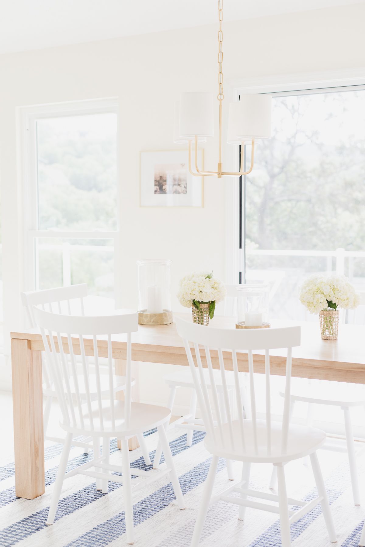 A teak dining table with white chairs on a blue and white striped rug