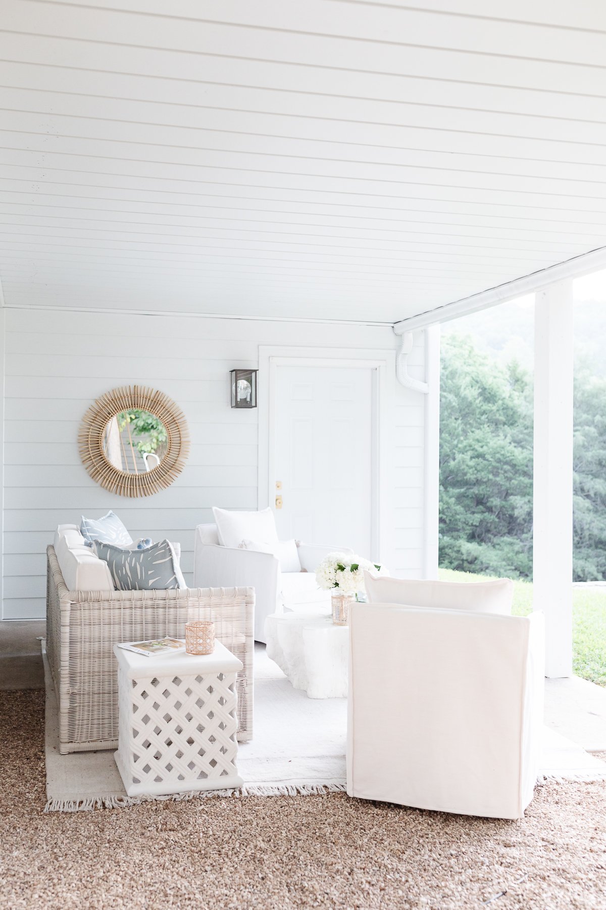 A white covered porch with wicker furniture and ceramic garden stools.