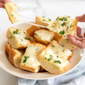 A person pulling apart a piece of cheesy garlic bread, an Italian side dish, with melted cheese stretching between the slices.