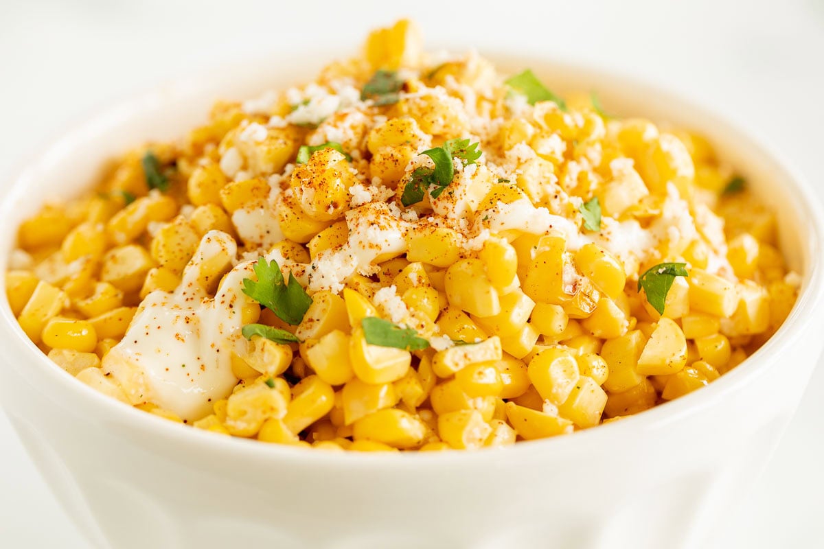 A close-up of a bowl filled with seasoned corn kernels, topped with crumbled cheese, cilantro, and a sprinkle of spices. Perfect for lovers of Mexican side dishes.