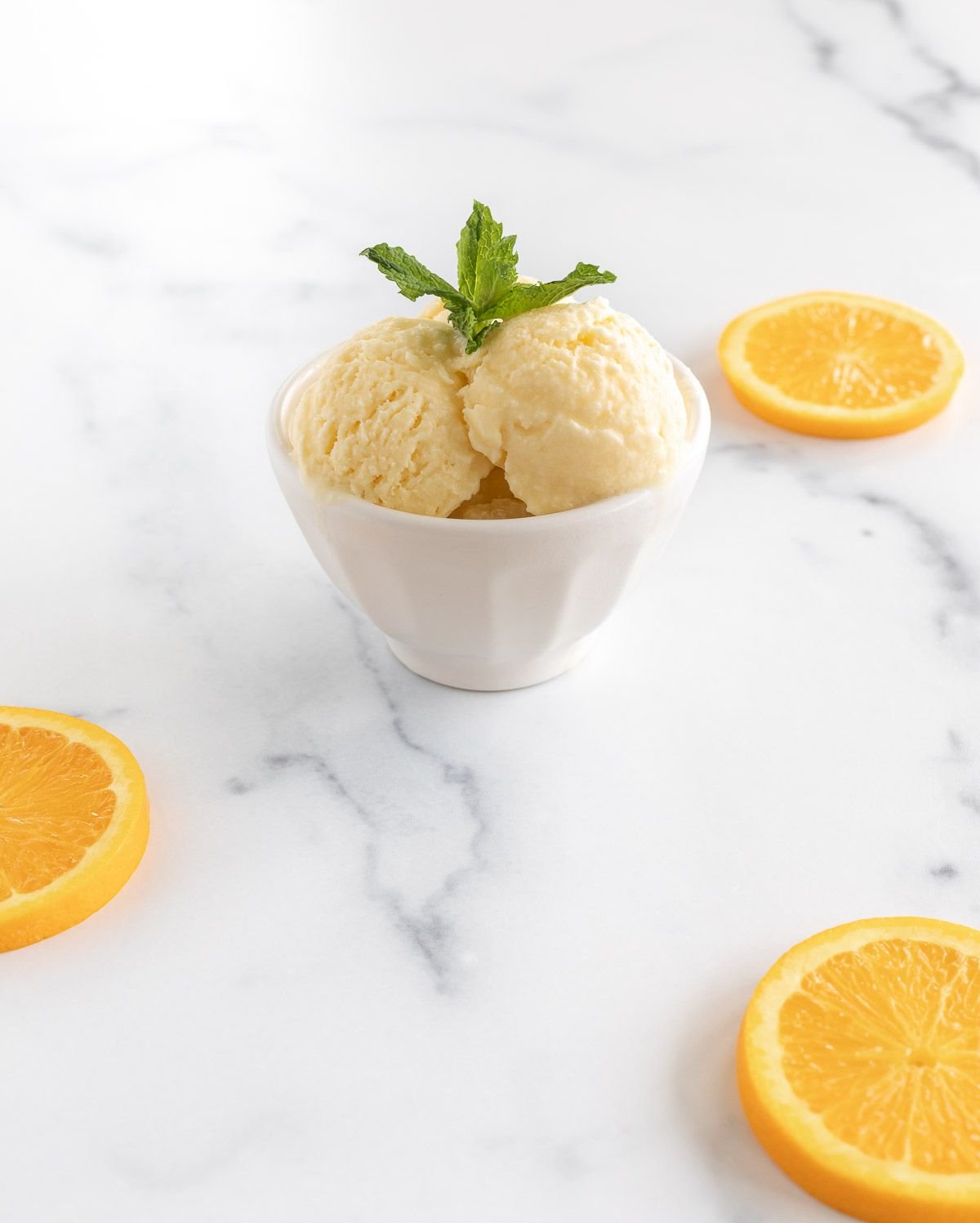A small white bowl full of orange sherbet on a white surface