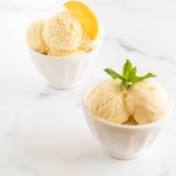 Two small white bowls full of orange sherbet on a marble surface