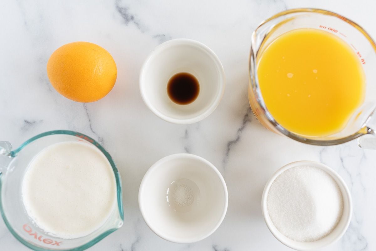 Whipping cream, vanilla and orange juice laid out on a marble surface