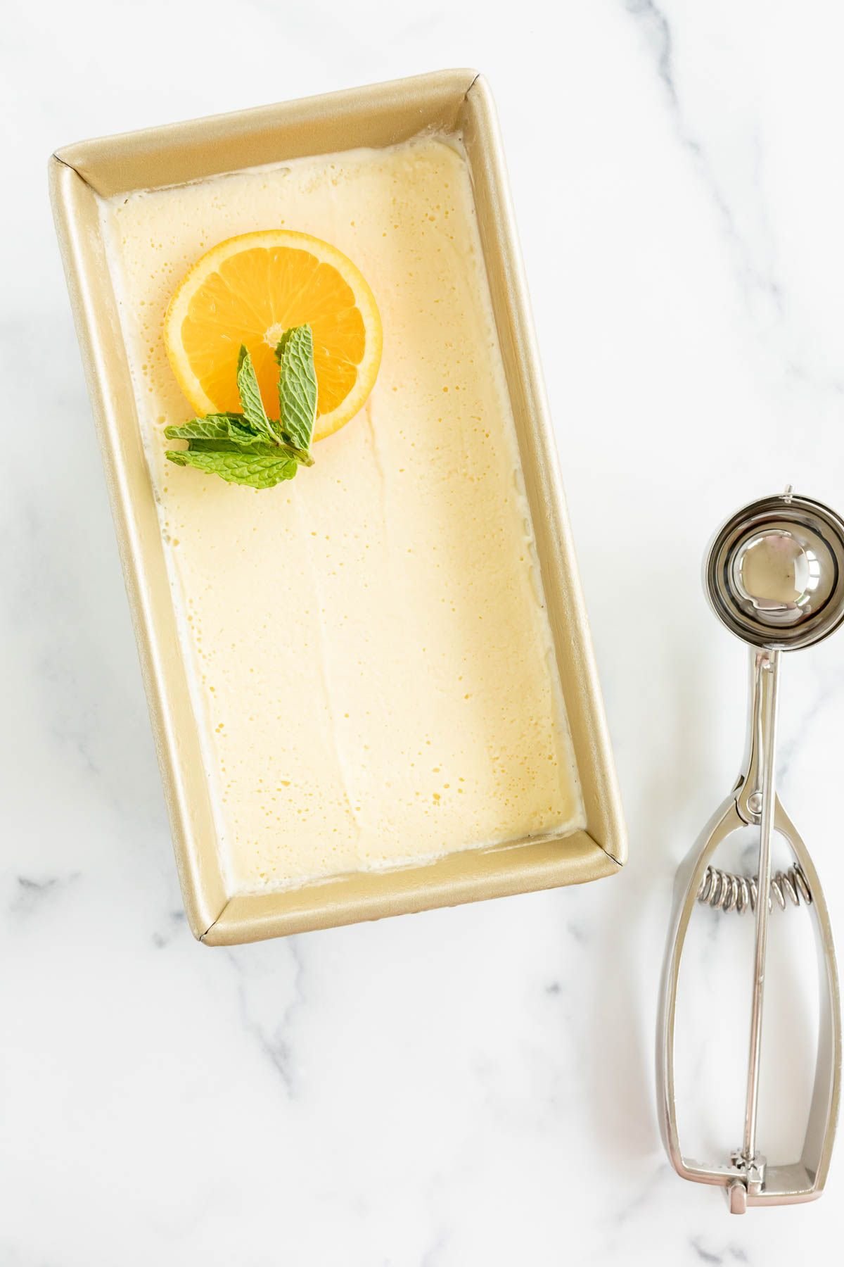 Homemade orange sherbet in a gold loaf pan, with an ice cream scoop