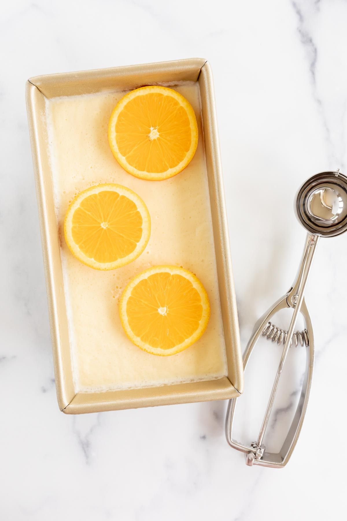 Homemade orange sherbet in a gold loaf pan, with an ice cream scoop