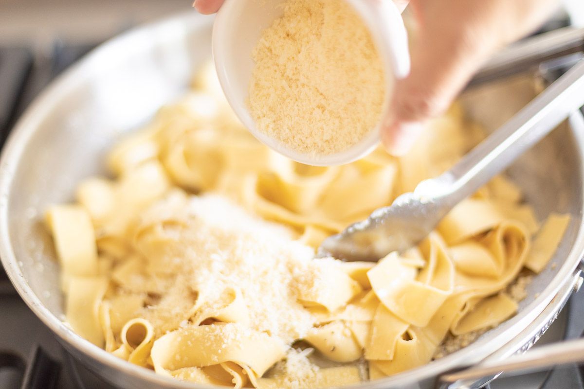 parmesan is added to a silver pan with noodles