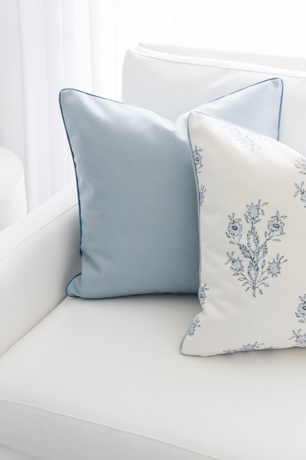 Dos almohadas decorativas en un sofá blanco; Uno es azul sólido, el otro presenta un patrón floral azul. Estas elegantes cubiertas de almohada de lanzamiento agregan un toque de elegancia a cualquier espacio habitable.