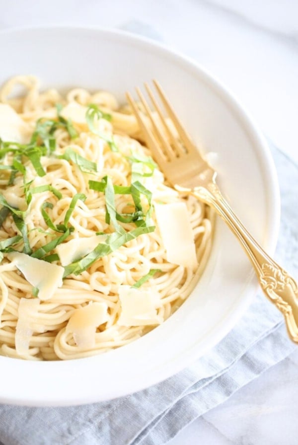 A plate of pasta garnished with cheese shavings and fresh herbs, accompanied by an ornate gold fork, perfect as a side dish to salmon.