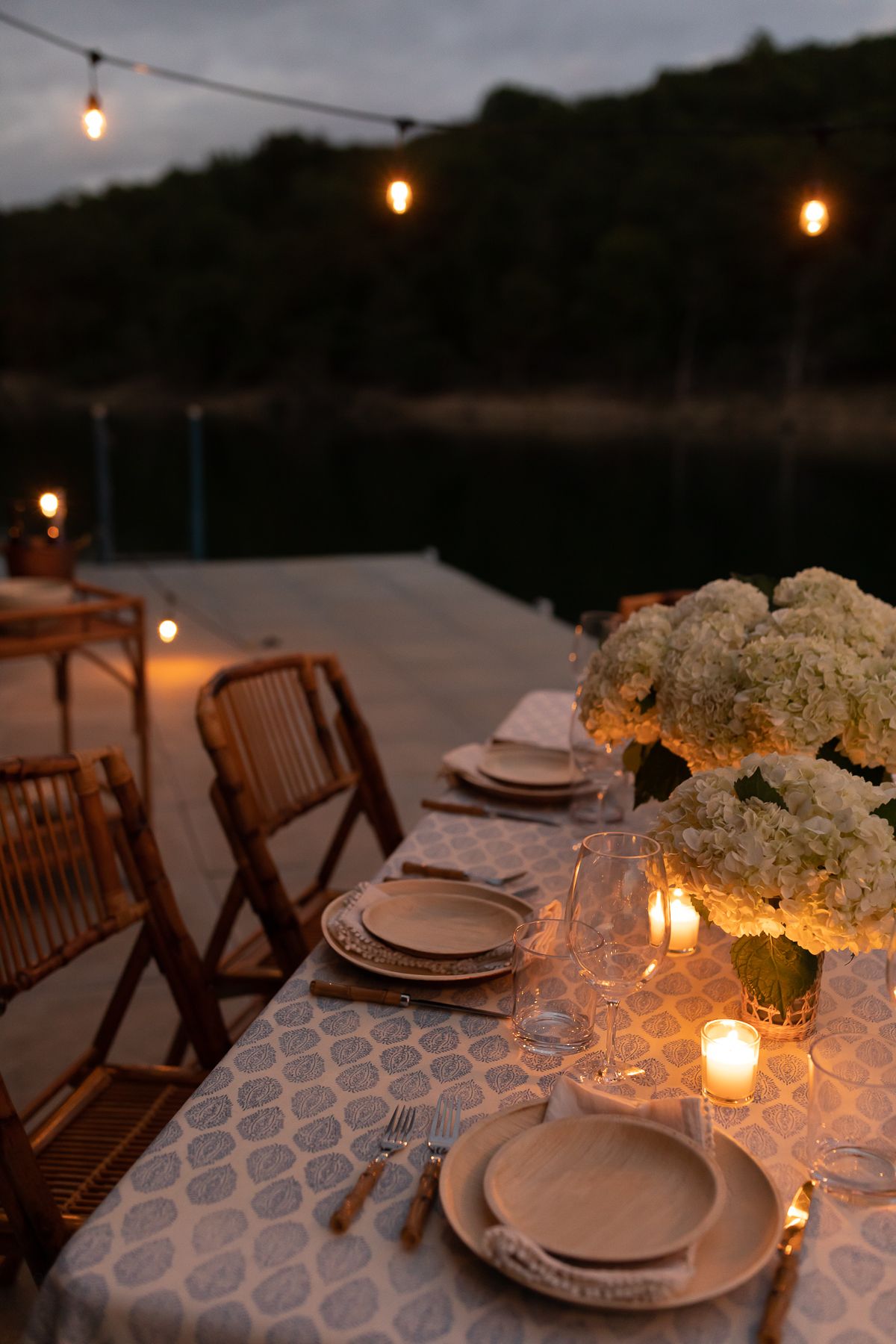 outdoor string lights set up over a dining table on a dock, water in the background