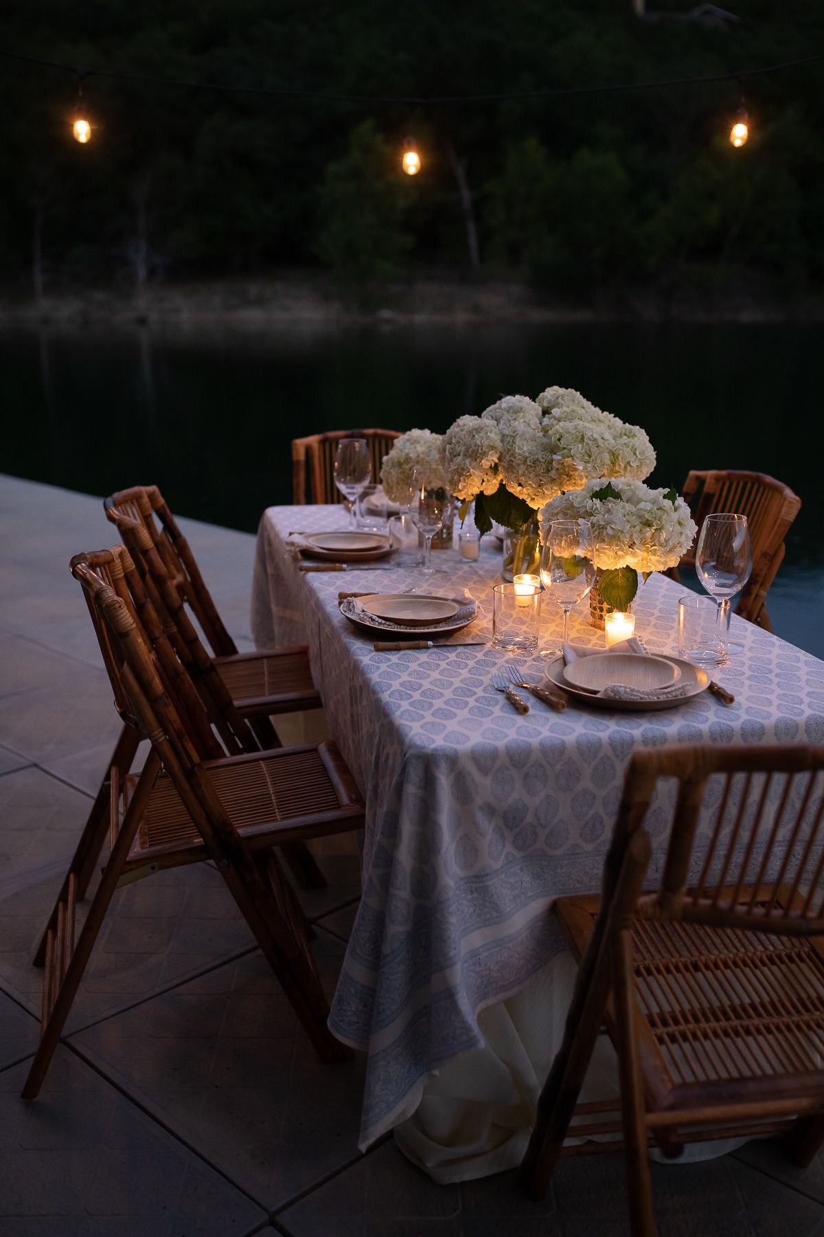 outdoor string lights set up over a dining table on a dock, water in the background