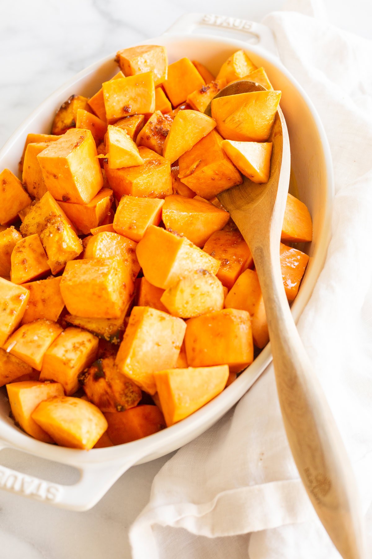 A white dish filled with cubed sweet potatoes, a delicious option for healthy steak sides, accompanied by a wooden spoon.