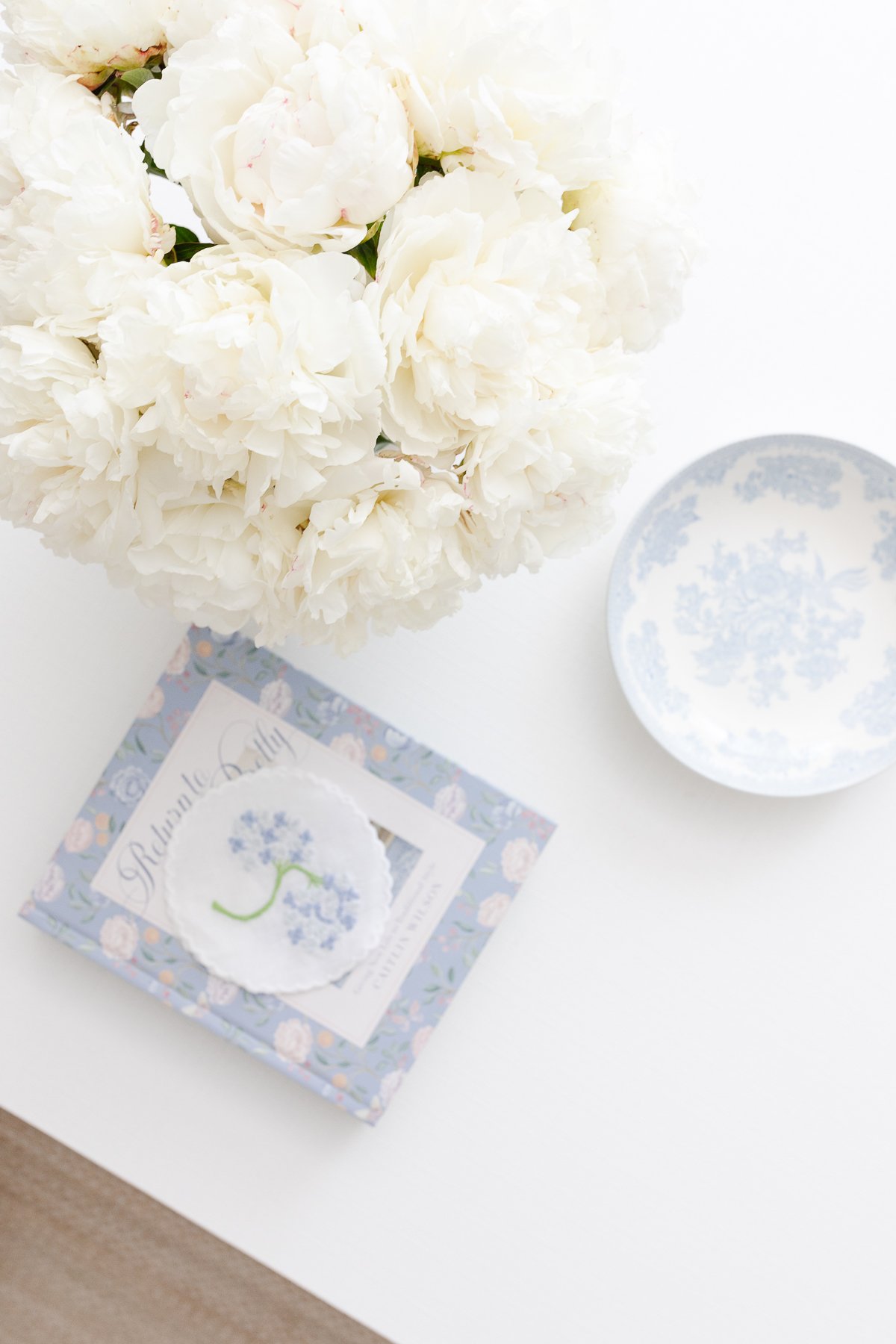 A coffee table featuring white flowers and a blue and white coffee table book.