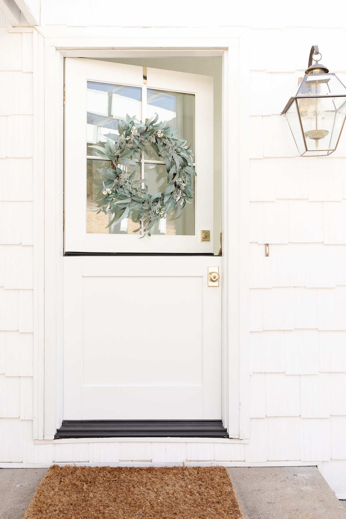 A white dutch door on the front of a cottage with brass door handles