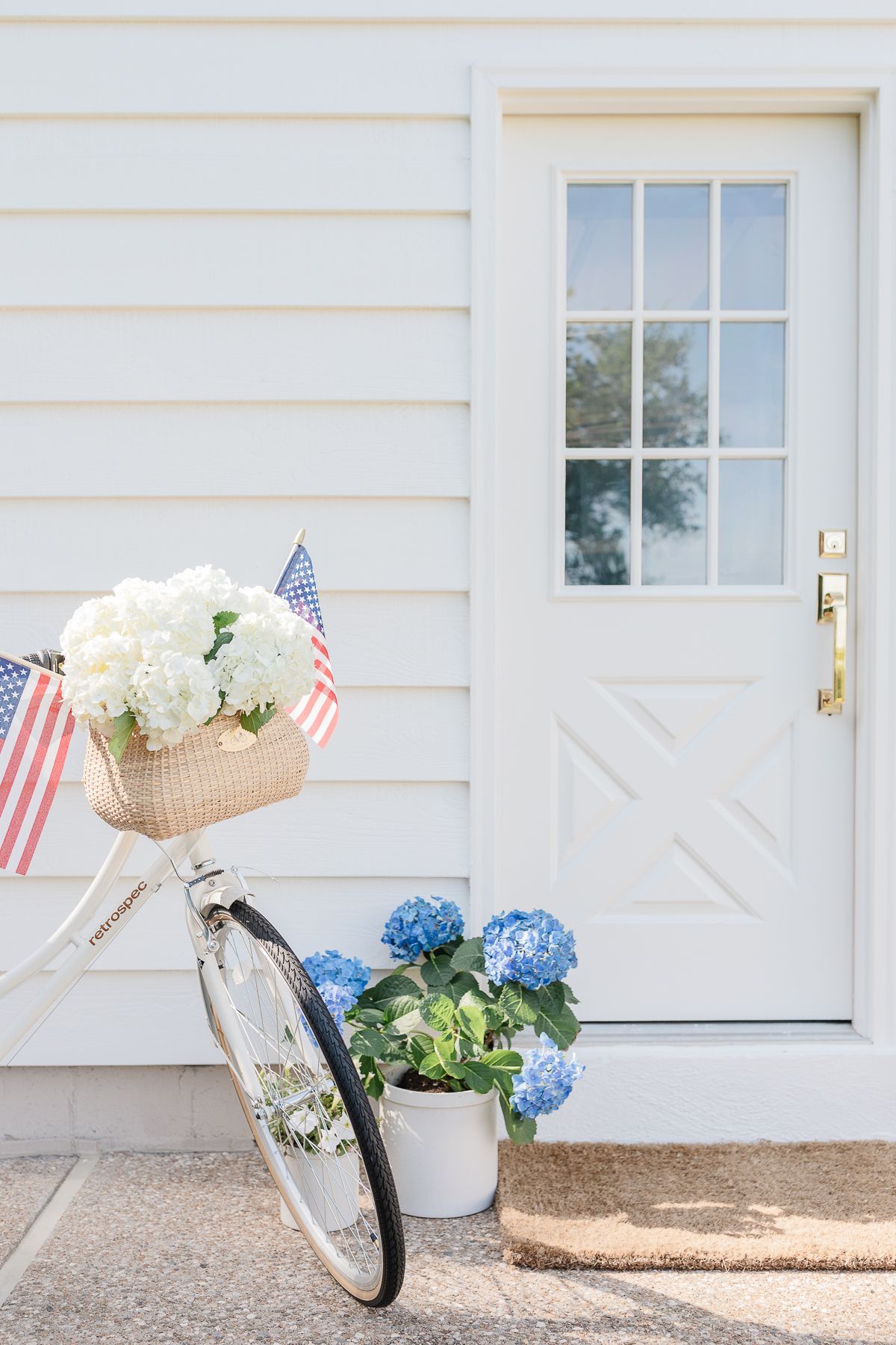 A white biked decorated for the 4th of July, parked in front of a white door with a brass exterior door handle