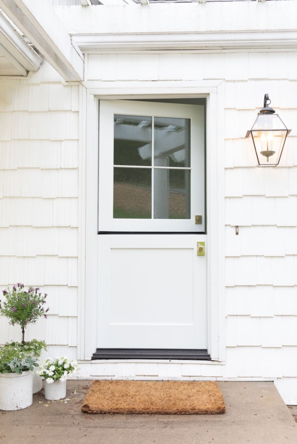 A white dutch door on the front of a cottage with brass door handles