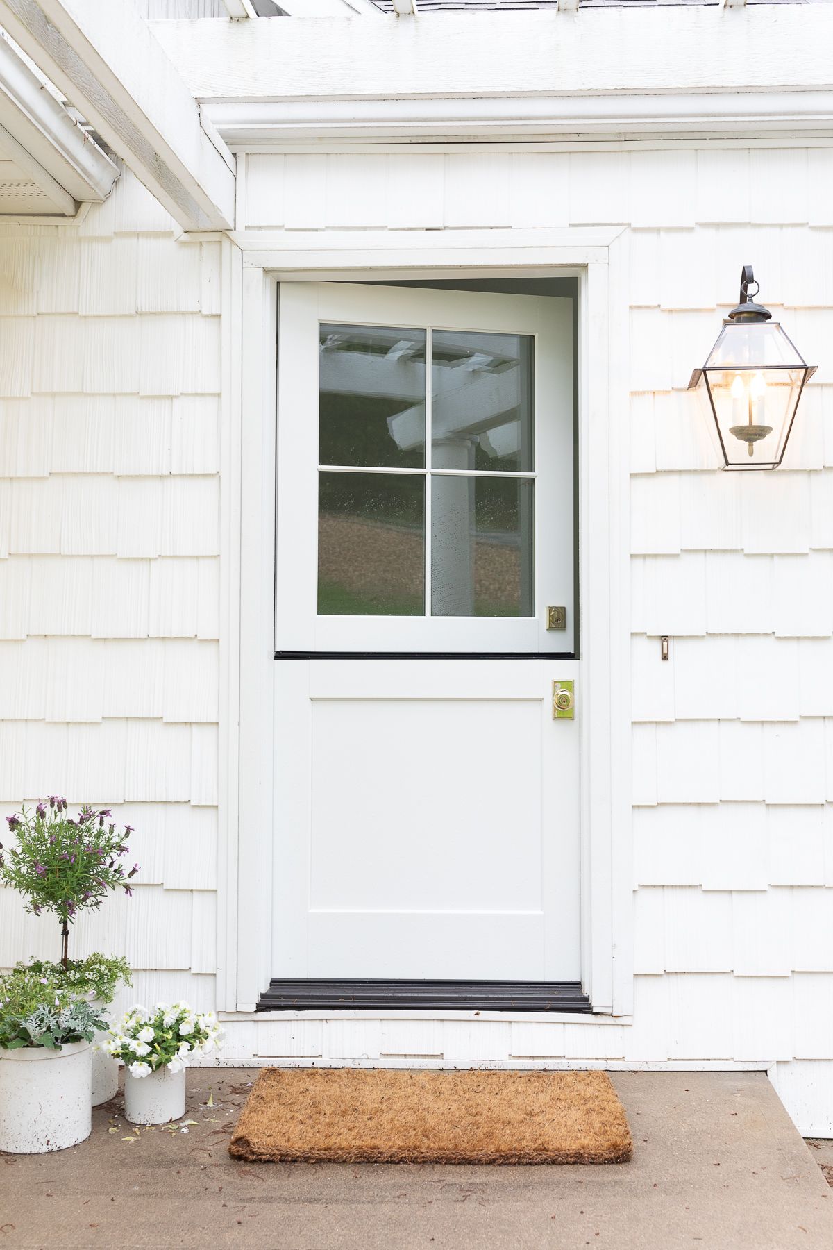 A white dutch door on the front of a cottage with brass door handles